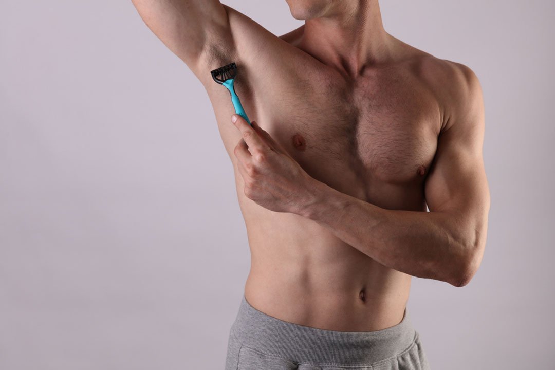 man using razor to shave armpit